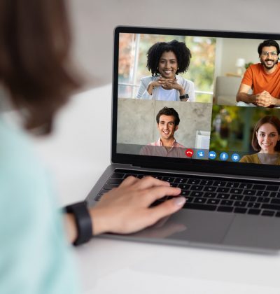 Millennial caucasian businesswoman in suit at table with laptop with different people on screen in office interior. Remote meeting, video call, business, work, website and social networks